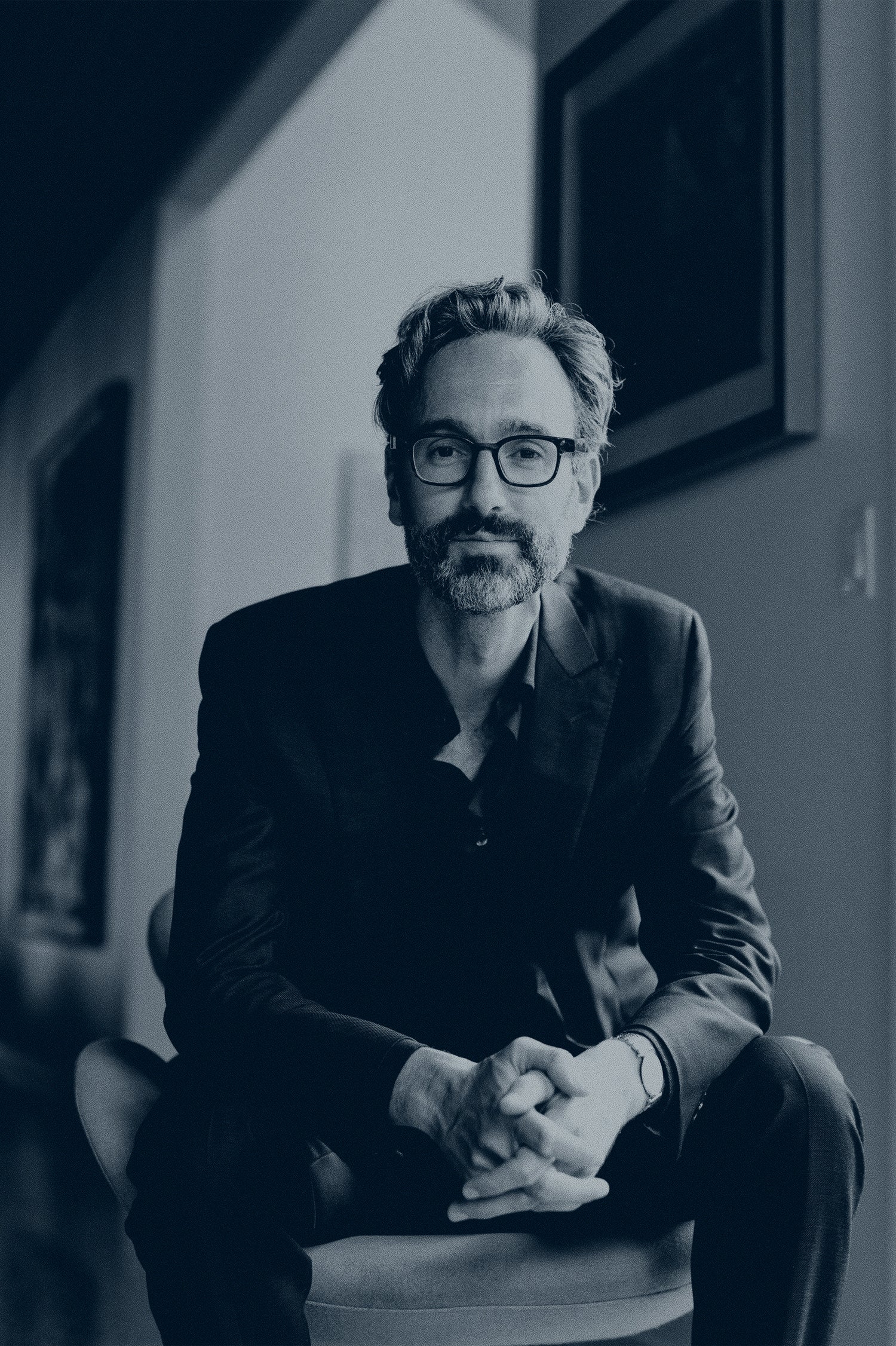 Black and white image of David Myles in Nova Scotia on an arm chair leaning forward onto his knees.