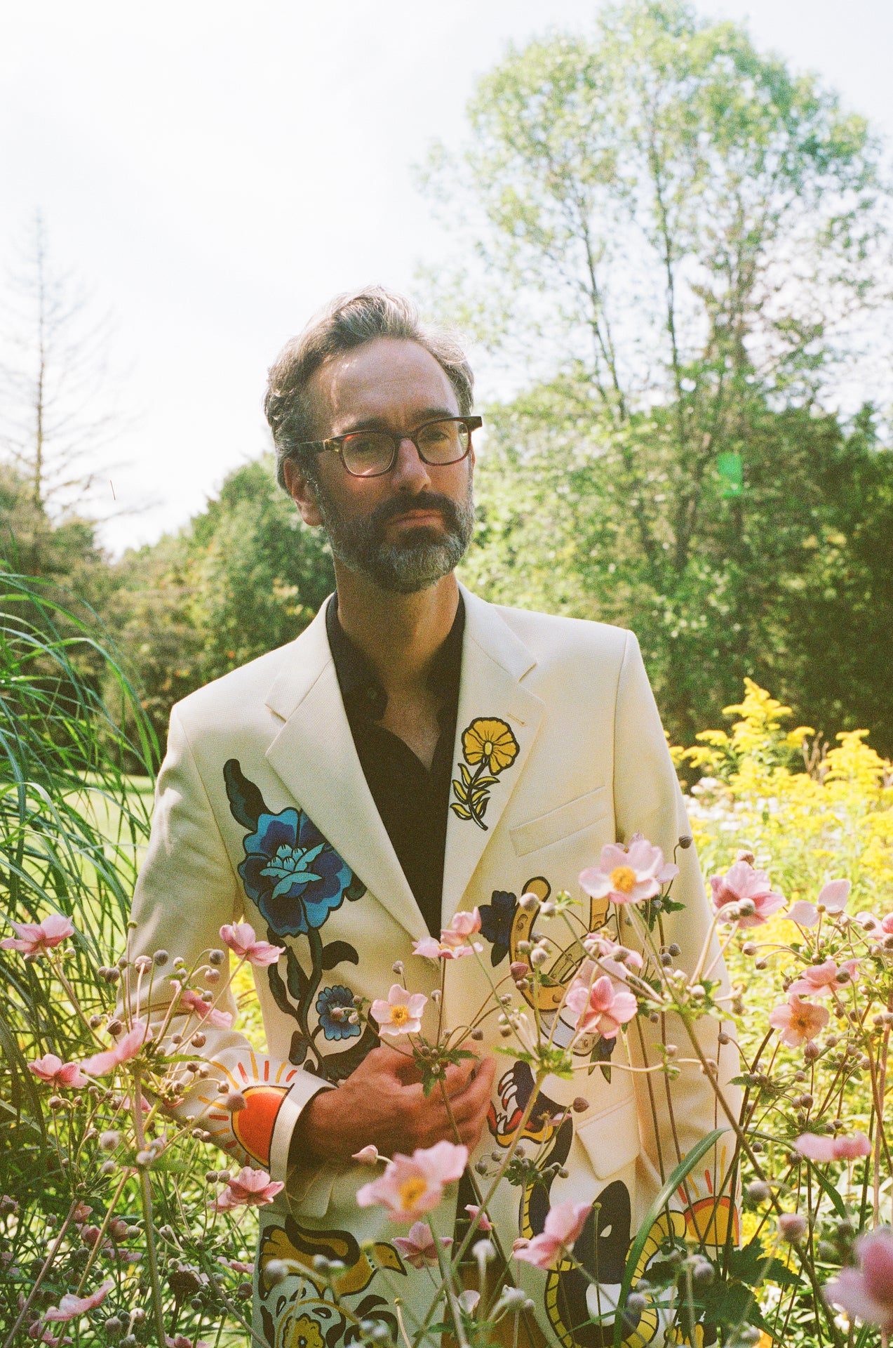 David Myles standing in Nova Scotia Canada in a field of flowers wearing a white jacket with a floral design on it.